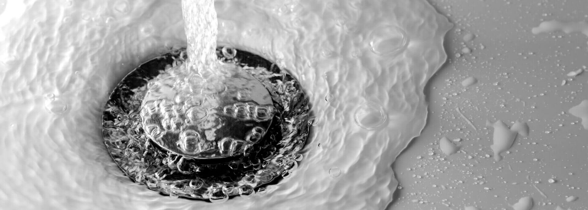 Water Drains Into The Hole Of White Sink In The Bathroom