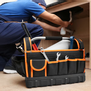 Plumber With Set Of Tools Repairing Sink In Kitchen