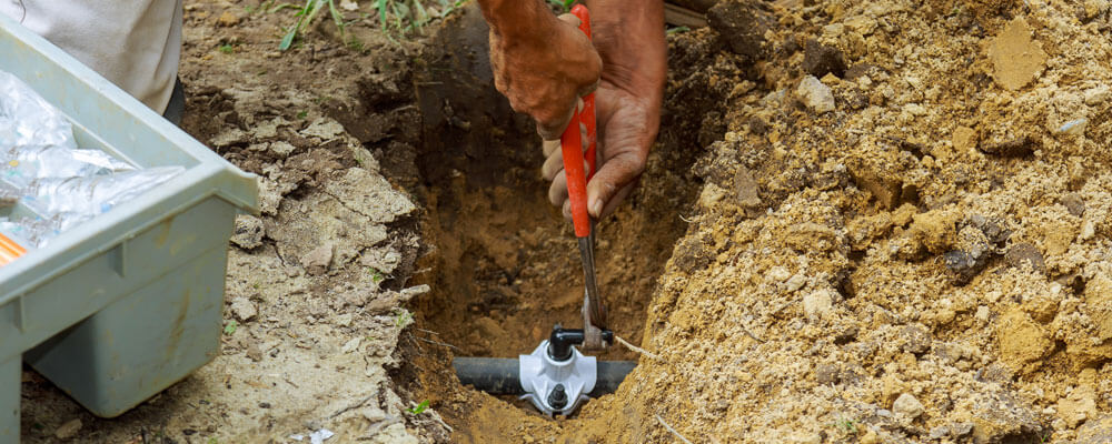 Man Working With Pipes In Ground While Installing A New Underground Sprinkler System